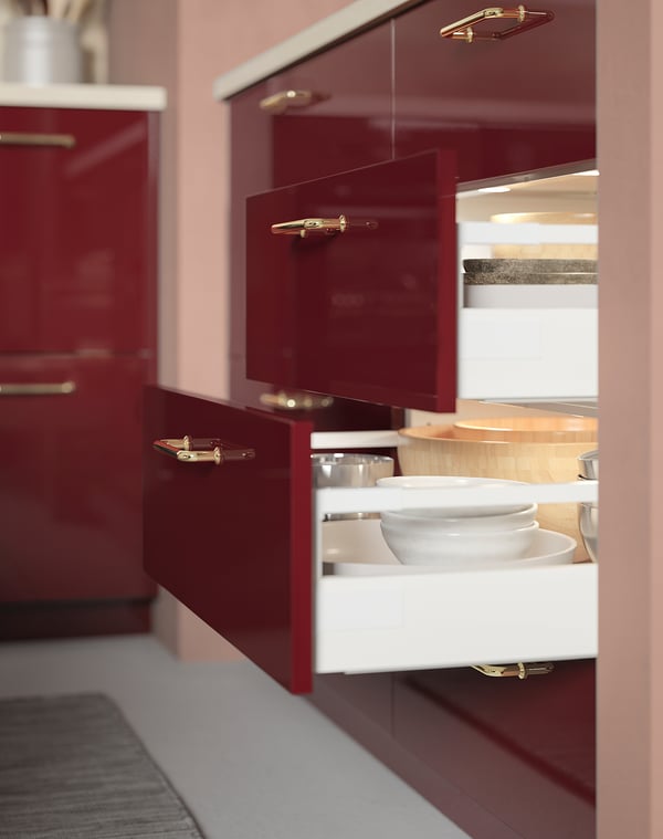 Modern kitchen with red cabinets, led lights above white drawer of stacked bowls.