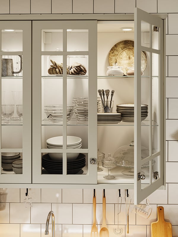Modern kitchen cabinet with glass doors, lit by MITTLED light, displaying plates, bowls, and glasses, organised and visually appealing.