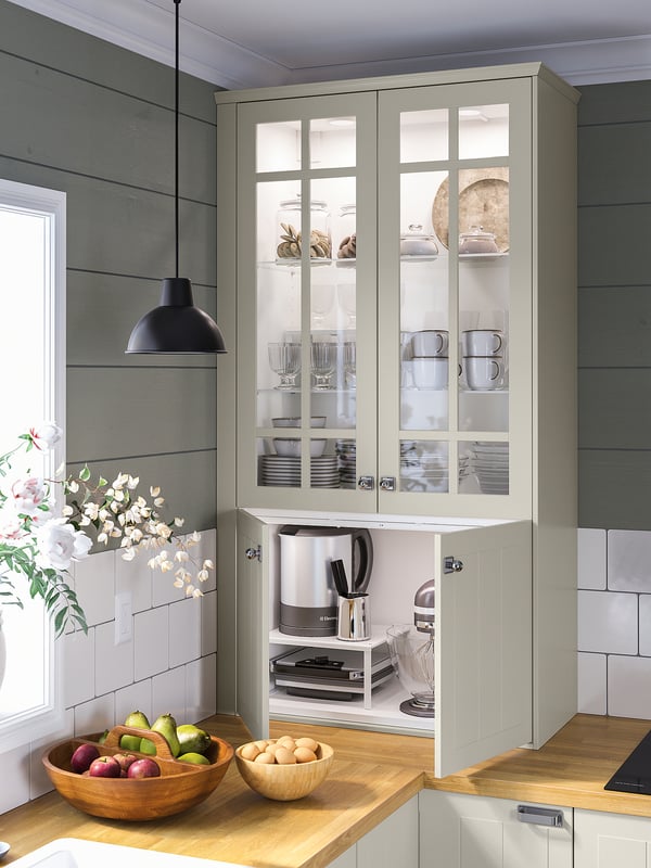 Modern kitchen with MITTLED light, white. Glass cabinet displays dishes. Wood counter holds fruit bowls.