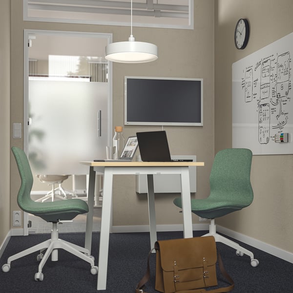 Modern office with mitzon white table, green chairs, laptop, brown bag, wall tv, notes, clock.