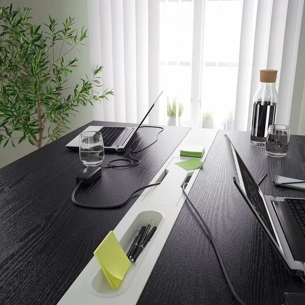 Conference table with integrated footrest and cable management, perfect for sitting or standing meetings. Pens and glasses are placed on the table.