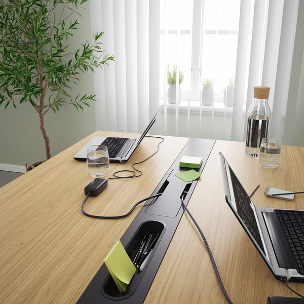 Conference table with cable management, laptops, drinks, plant.