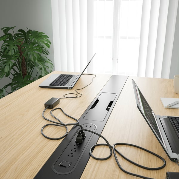 Modern wooden conference table with integrated power strips and cables, promoting efficient meetings. A large plant adds natural decor.