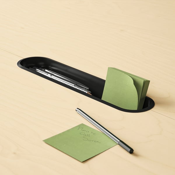 Black pen tray holding pens and green sticky notes; one note reads please call goren.