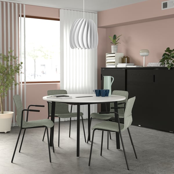 Round MITTZON conference table with 4 green/black chairs, white, perfect for small meetings, surrounded by cabinet & plants.