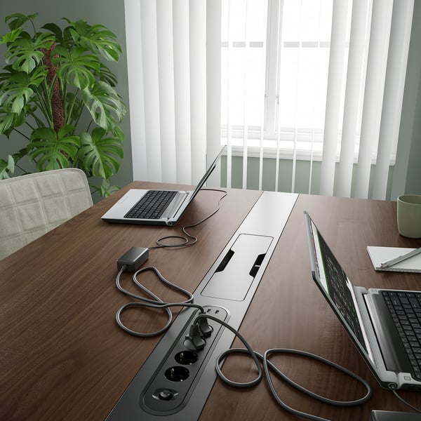 Conference table with laptops and power outlets. Perfect for meetings, with built-in cable management. Green chair and plant nearby.
