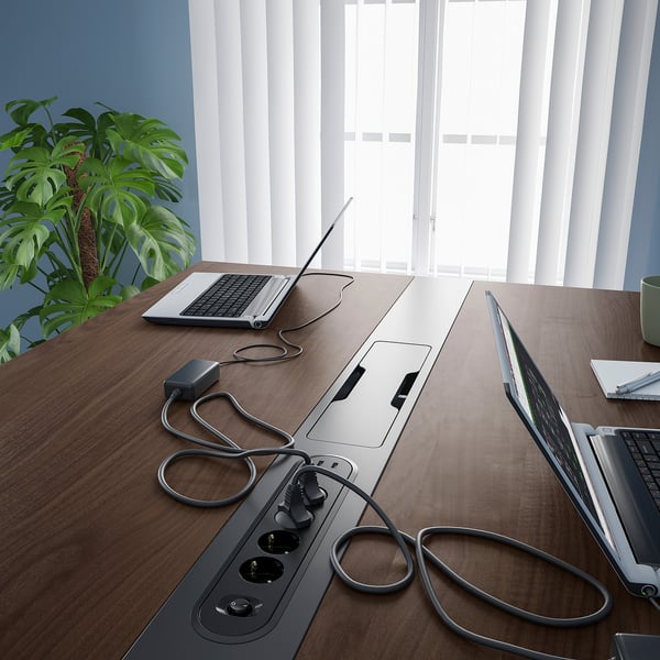 Modern conference table with built-in power outlets and cable management, ideal for meetings. Laptops and cords visible on the table.