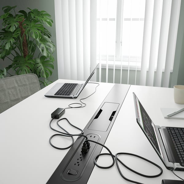 Conference table with multiple laptops, power strips, and cables for collaborative work.