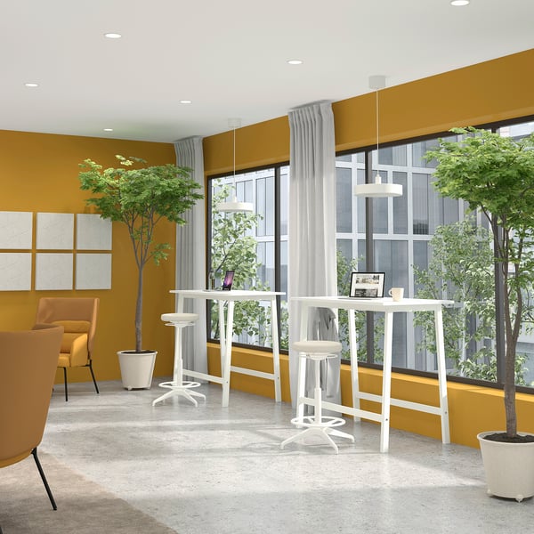 Bright yellow room with MITTZON high tables, stools, orange chairs, potted plants. Large windows with sheer curtains. Modern minimalist design.
