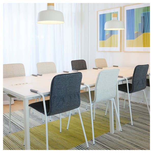 Modern conference room with MITTZON table, white chairs, colourful rug, abstract art, and pendant lights.
