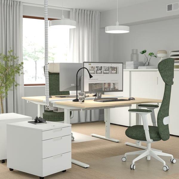 Modern home office with MITTZON desk, green chair, large screen, and accessories. Bright room with big windows.