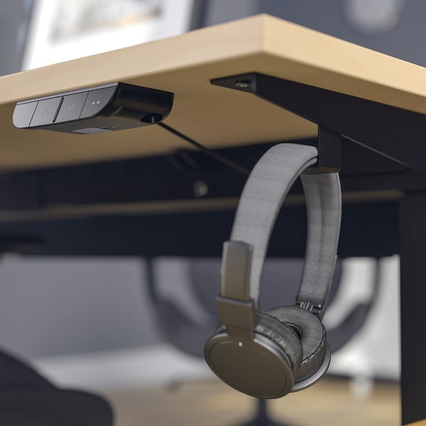 A modern desk with a motorised sit-to-stand feature, hanging headphones, and a control panel.