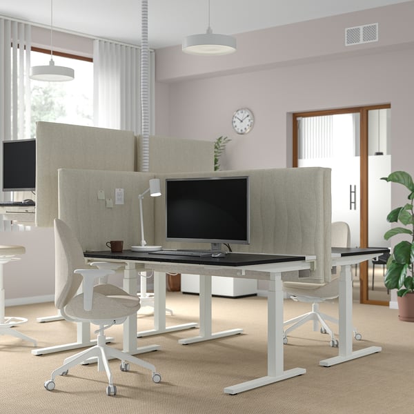 Office workspace with MITTZON sit-stand desks, light beige, modern, and ergonomic. Dual monitors, chairs, plants, and large windows.