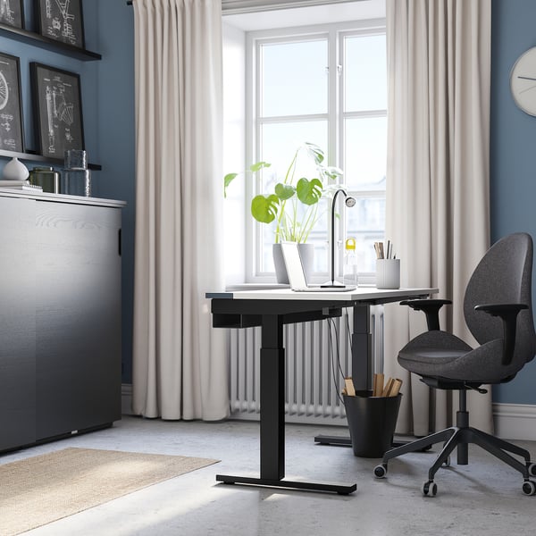 Home office: black MITTZON height-adjustable desk by window, grey chair, potted plant, laptop, and shelves.