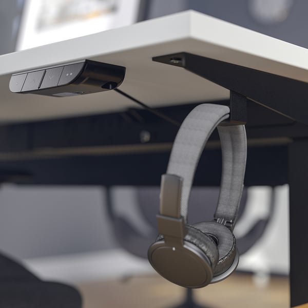 Desk with dual motors, memory settings, and cable management tray. Headphones hang on hooks.