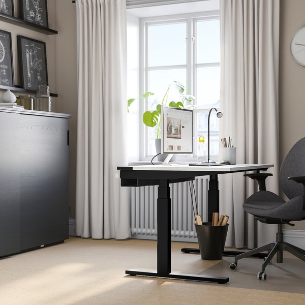 Minimalist office with MITTZON desk, monitor, keyboard, lamp, plants. Grey chair, dark organiser, white walls, large window.