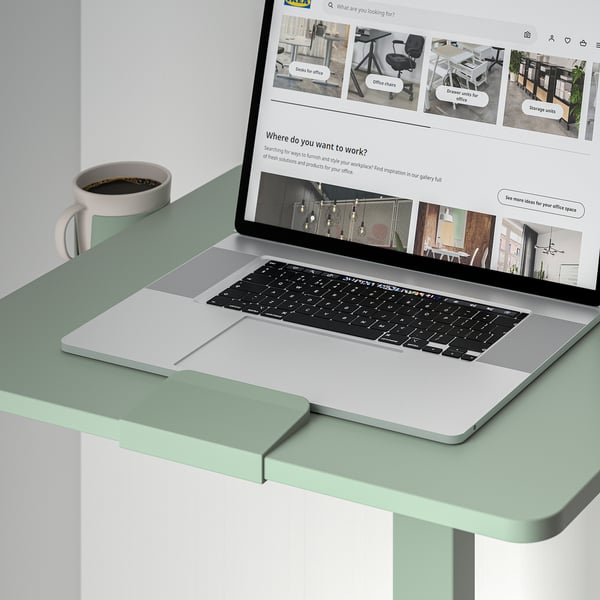 Laptop on adjustable desk with coffee cup, displaying office furniture website.