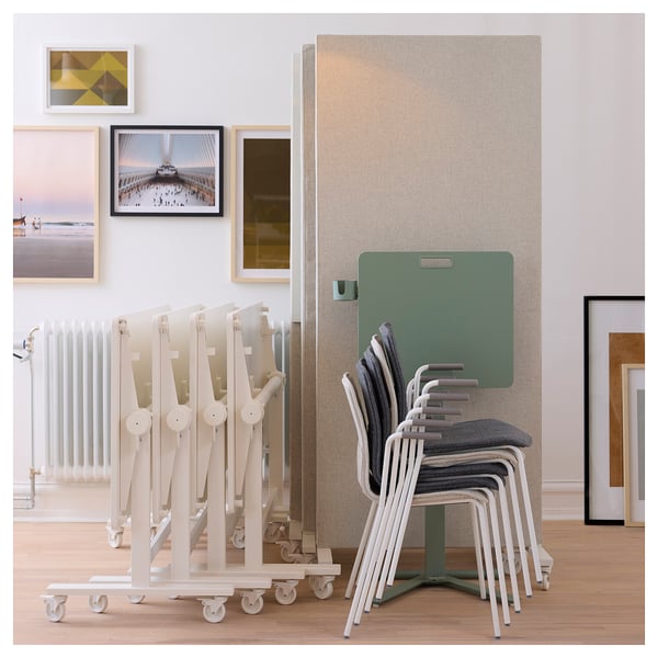 Stacked MITTZON laptop tables and chairs near wall art. Tables are white, height-adjustable with a green top. Chairs are white and grey.