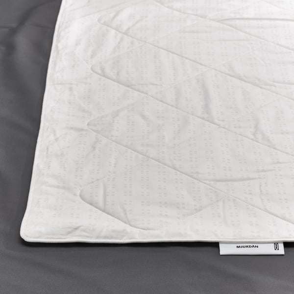 Close-up of a white silk-filled duvet on a dark background, showcasing its soft, luxurious texture. Ikea label visible.