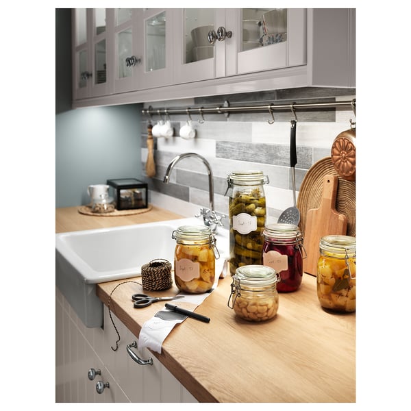 Kitchen counter with oak wood top, glass jars with preserved foods, sink and utensils.