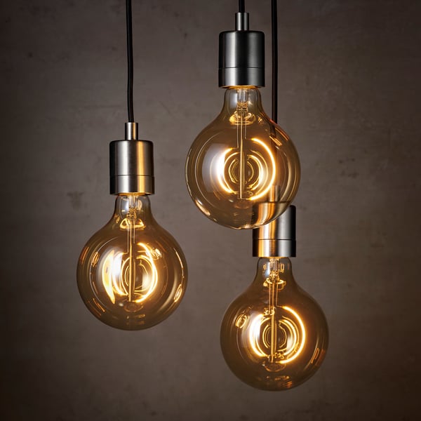 Three vintage-style light bulbs with clear brown glass and spiral filaments hang from black cords, emitting a warm, soft glow.
