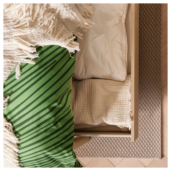 Green striped rug beside tan cushions and woven mat.