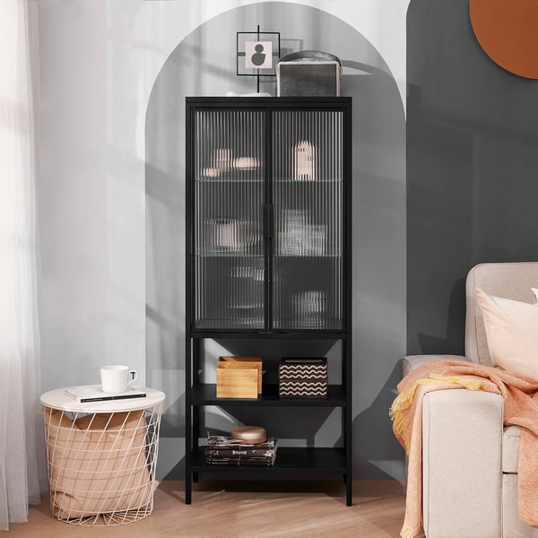 Black MOSSJÖN cabinet with textured glass doors and open shelves, holding decor, beside a small table and chair.