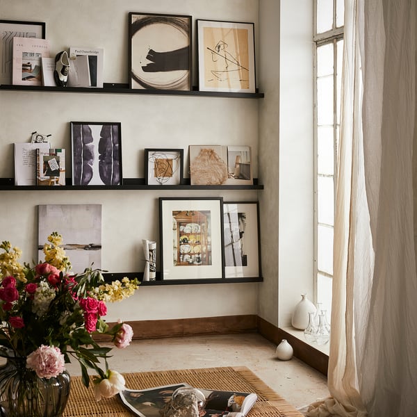 Modern room with MOSSLANDA black picture ledges displaying abstract art and vibrant flowers near a window.