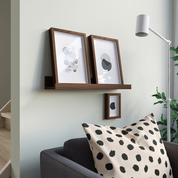 Wooden shelf with 3 abstract prints over grey sofa, white lamp.