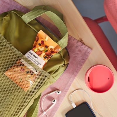 Open green bag with MUNSBIT snack, earphones, phone, and red object on wooden table.