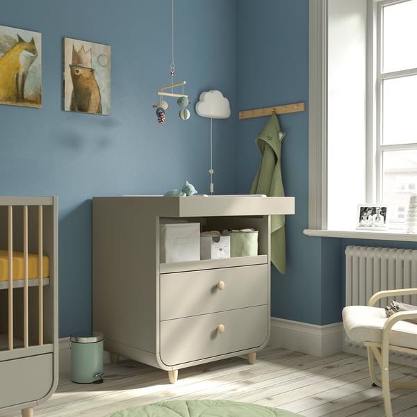 Light blue MYLLRA changing table with drawers, removable front, between crib and radiator.