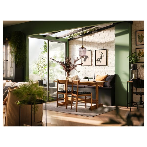 A cosy dining area with a wooden NACKANÄS table and chairs in a bright room with green walls and white brick.