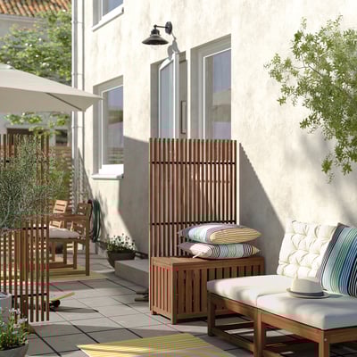 Modern outdoor patio with brown acacia wood furniture, striped cushions, and greenery.