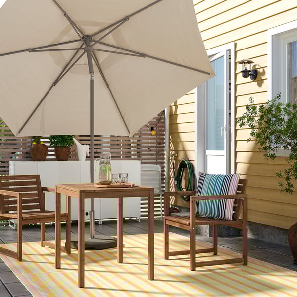 Cosy patio with umbrella, table, chairs, and rug beside a yellow house.