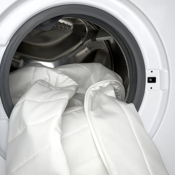 A white mattress pad inside a washing machine, highlighting its washable cover for easy cleaning.