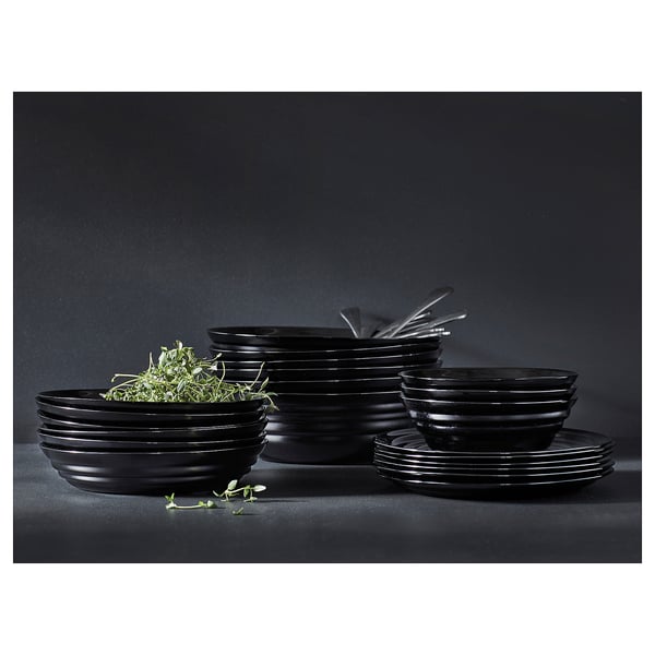 Black tempered glass dinnerware set, including bowls, plates, and dishes, arranged neatly with herbs on dark background.