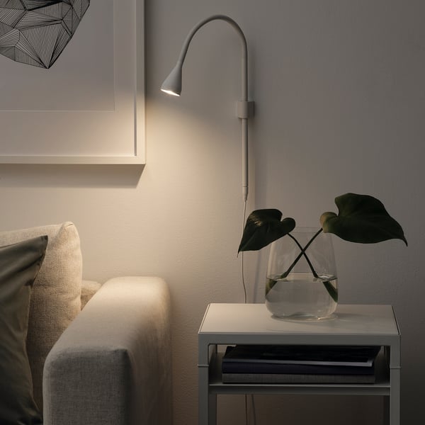 Grey NÄVLINGE wall lamp illuminating side table vase.