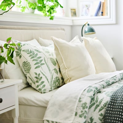 Bed with NÅLBJÖRNBÄR duvet: white, green floral, recycled cotton/viscose. Large pillows, plant nearby.