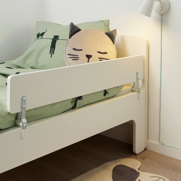 Childs bed with white railing to prevent falling. Cat-themed pillow and green blanket are visible.