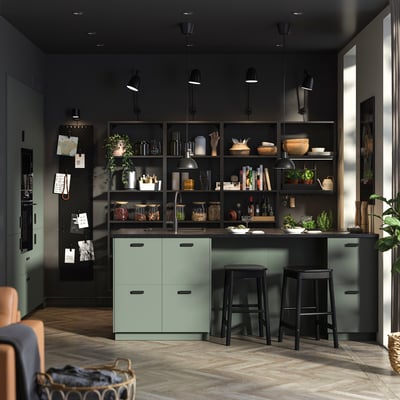 Modern kitchen with dark walls, green cabinets, open shelves with plants and dishes, black bar stools.