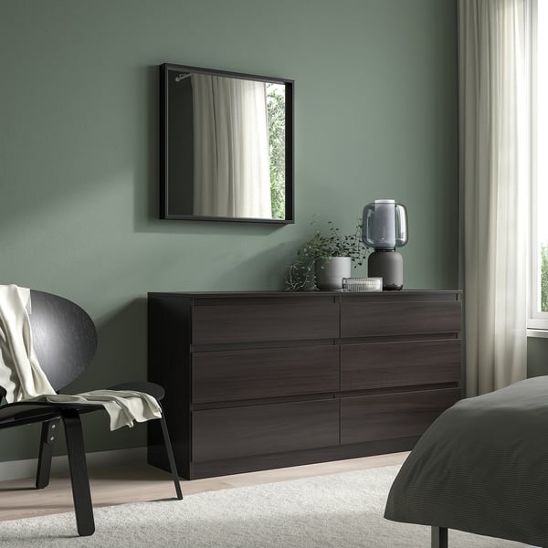 Modern bedroom with NISSEDAL mirror, chest, plants, lamp, chair & blanket against sage walls.