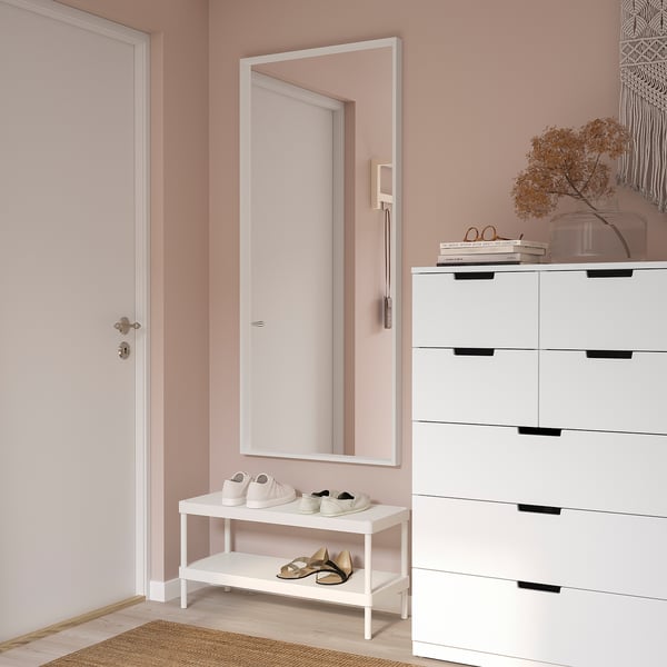 A NISSEDAL white rectangular wall mirror, larger than the shoe rack and dresser beside it, hung vertically on a pink wall in a hallway.