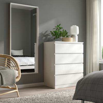 Modern bedroom with NISSEDAL white dresser and mirror. Dresser topped with plant and lamp, mirror reflects bed.