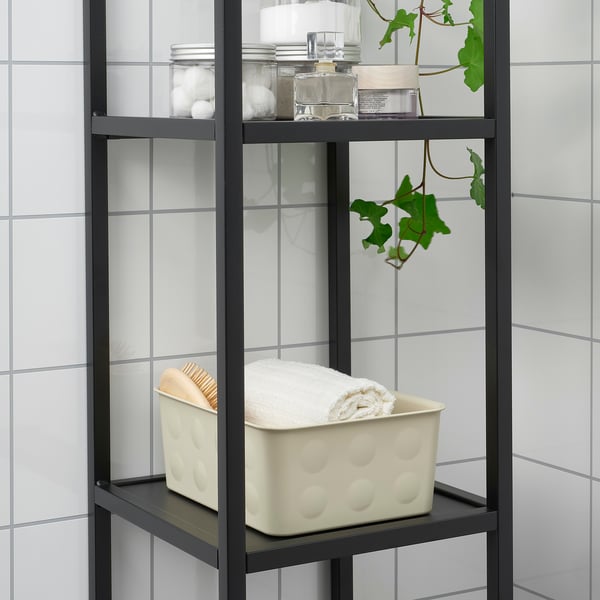 Black metal shelf with white container storing towels, jars, and plant against white tiled wall.