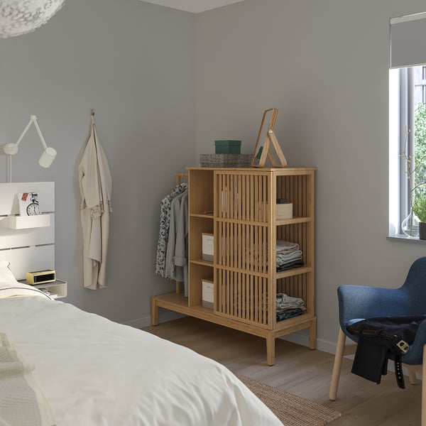 Minimalist bedroom with NORDKISA wardrobe, coat hook, blue chair, and bed with white sheets.