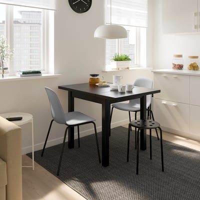 Modern dining area with NYMÅNE light, grey chairs, white cabinets, and natural light.