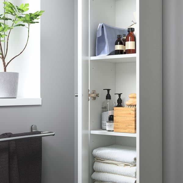Open bathroom cabinet with shelves holding towels, bottles, and a wooden box. Door can swing left or right.