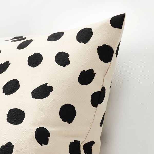 Black and white polka dot cushion cover, scattered dots on light background, visible stitching and zip detail.