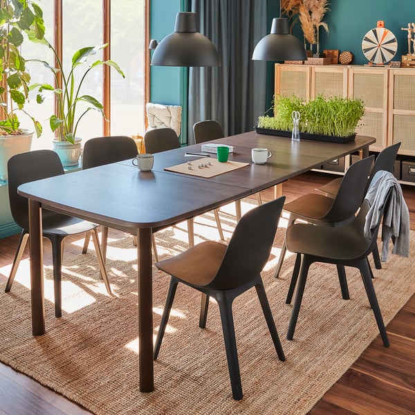 Cosy dining room with modern grey chairs and extendable table, hanging lights, plants, and natural decor.