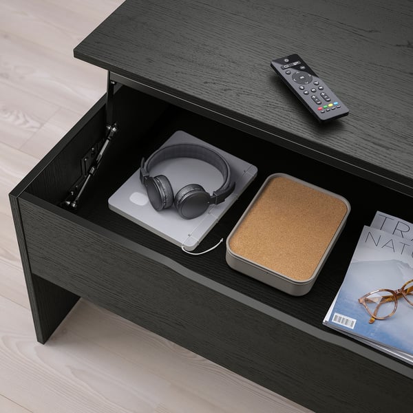 Dark wood coffee table with adjustable height, storage, and cable management. Headphones, laptop, remote, and magazines shown inside and on the table.